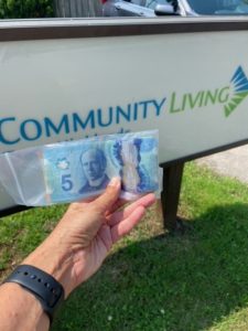 Hand-holds-cash-in-front-of-community-living-sign